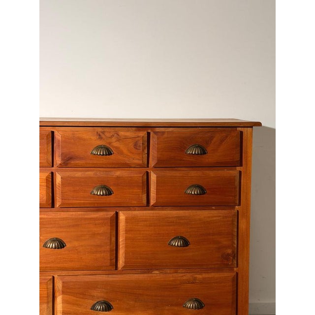 A distinctive wooden chest featuring warm honey-brown tones, expressive wood grain and dark metal shell handles. Its...