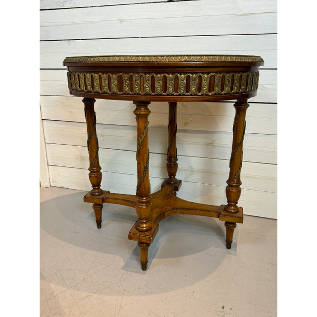 An elegant vintage oval side table dating to circa 1940s, featuring beautifully detailed marquetry accented by decorative...