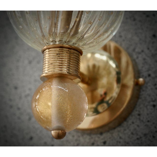 This transparent gold Murano glass wall light features a refined and delicate design. The wall light features a brass...