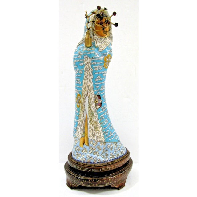 This antique Asian blue cloisonne figurine holding a brass vase with a lotus wood base stands at a height of 10.25 inches....