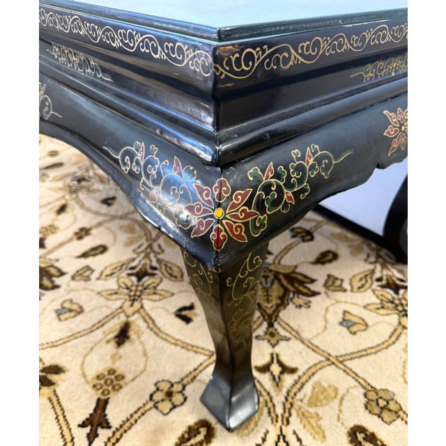 Striking chinoiserie black lacquered coffee table featuring intricate hand-painted gold detailing and an inset panel of...