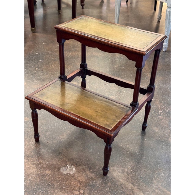 Two tiers, each inset with a leather panel worn to a soft greenish gold, make up these 19th century English mahogany...