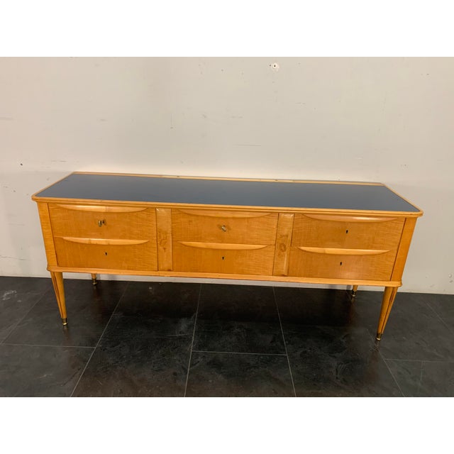 Maple chest of drawers, spindle legs with brass finials, and a blue glass top; the design is attributed to Paolo Buffa....