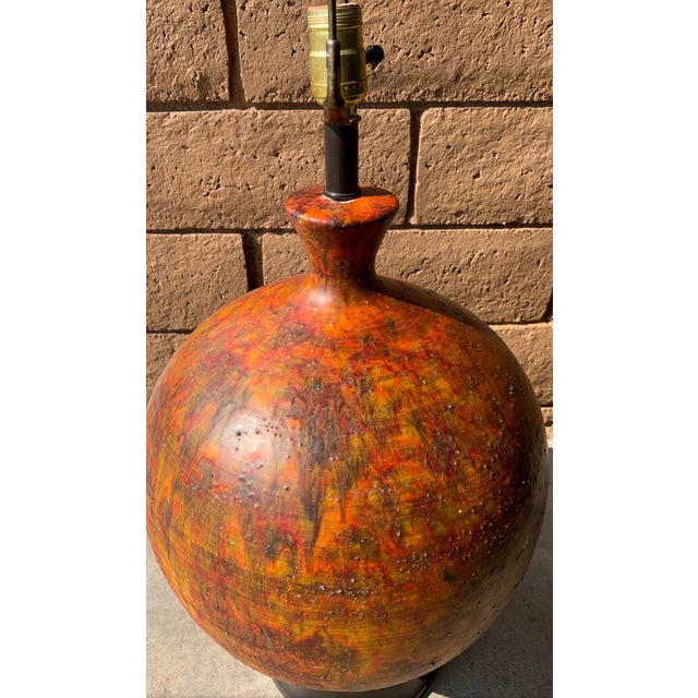 Mid century modern large pottery lamp. Rounded ceramic with abstract dark red orange textured paint. Wooden base. Harp is...