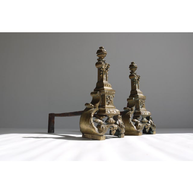 This stunning pair of antique brass andirons features exquisite openwork detailing and a rich baroque-style design....