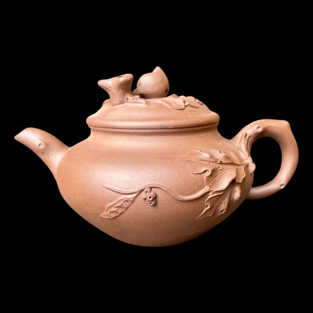An antique Chinese Yixing teapot crafted from rich brown terra cotta clay. The teapot features a naturalistic theme with...