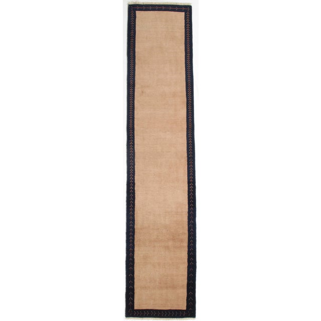 Vintage hand-knotted Persian Lori wool runner with a plain beige field framed by a dark border featuring simple linear...