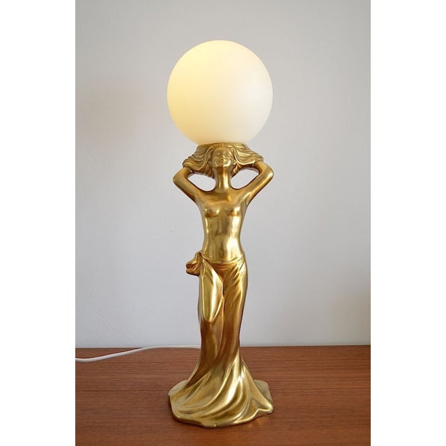 A figurative Hollywood Regency table lamp from the 1980s - The table lamp is made of ceramic and glazed with gold - The...
