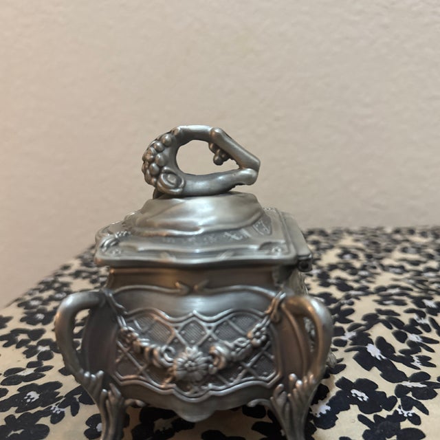 Featuring intricate floral and sunburst embossing, this footed casket is crafted in a classic Art Nouveau style. The lid...