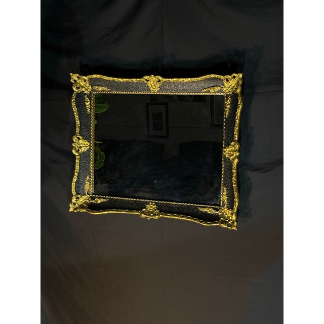 Ornate decorative wall mirror featuring a black frame with antique gold detailing and carved-style scrollwork. The piece...