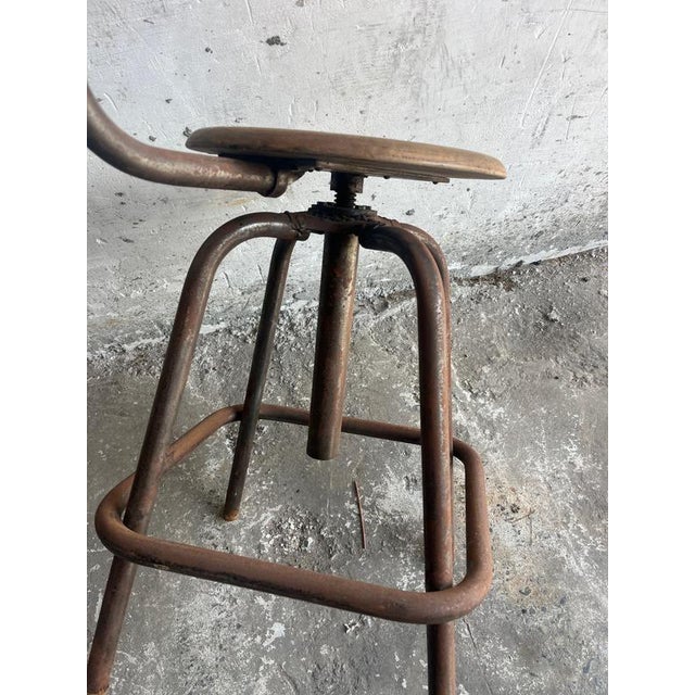 Authentic industrial workshop stool with adjustable height, wooden seat and backrest, and a patinated metal frame. The...