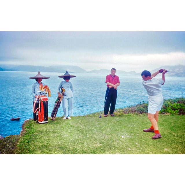 Hong Kong Golf by Toni Frissell A golfer tees off on a coastal course in Hong Kong, with two caddies and an opponent...