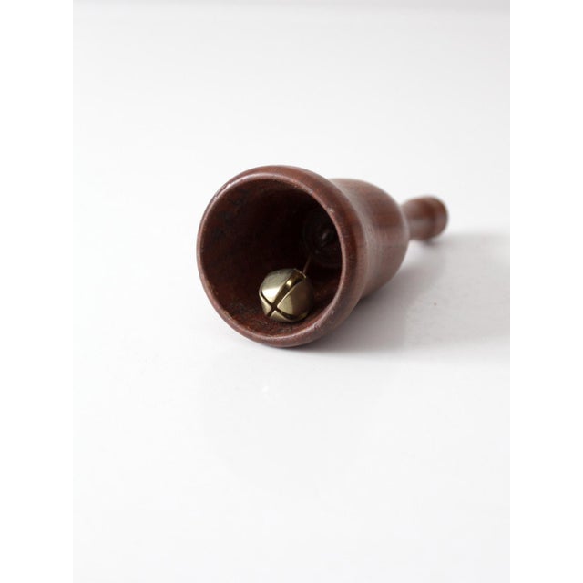 A turned vintage mid-century hand bell in warm natural wood, distinguished by its slender handle, gently flared bell, and...