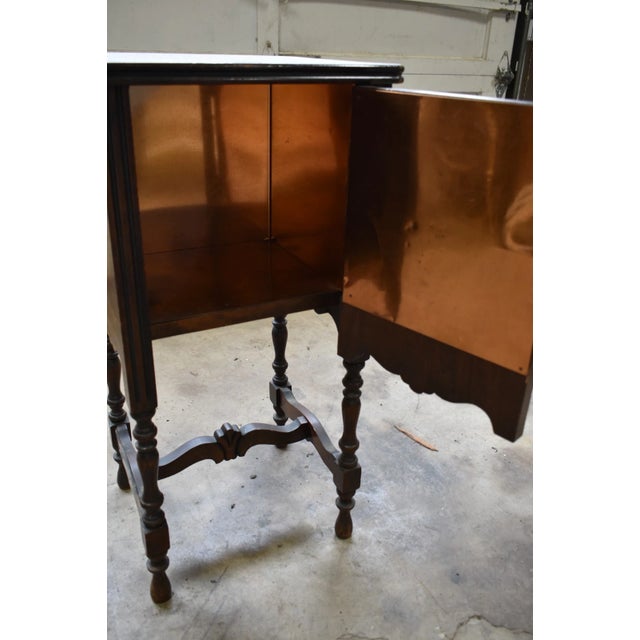 A charming antique smoking cabinet dating to the 1920s, featuring a beautifully carved wooden case and elegant turned...