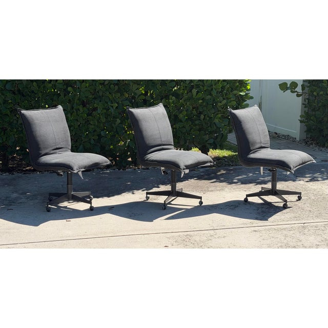 A set of three Restoration Hardware swivel desk chairs featuring sculptural, gently curved seats upholstered in charcoal...