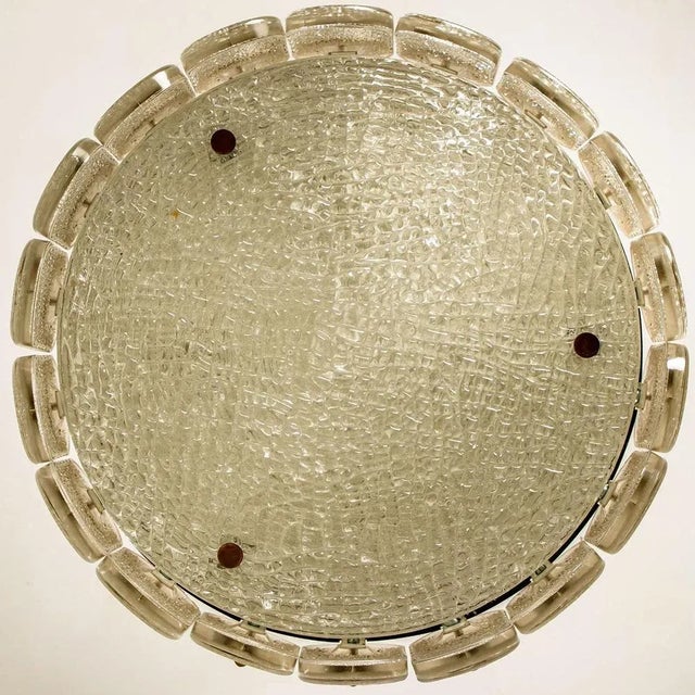 A glass fixture consisting of multiple pieces of textured glass hung around a textured glass plate with brass hardware by...