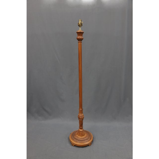 Wood stained floor lamp with knob and a carved laurel leaf pattern that wraps around the top of the base of the lamp....