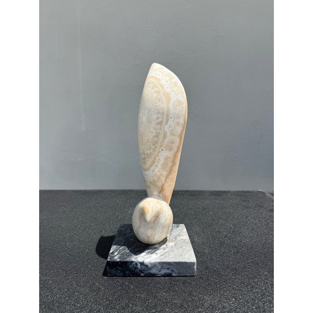 A sculptural abstract figure carved from richly banded cream onyx and mounted to a contrasting stone base. Defined by...