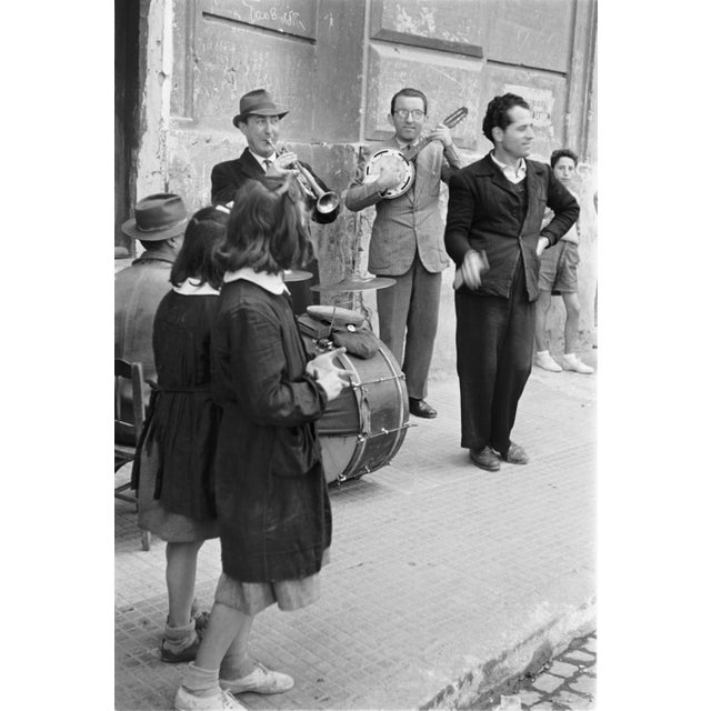 The black-and-white photograph captures a street scene in the Santa Lucia neighborhood of Naples, Italy, taken in 1954 by...