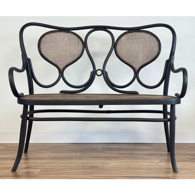 Unique vintage two seater bentwood settee bench featuring curved back, black stained frame and caned seat and back. Seat...