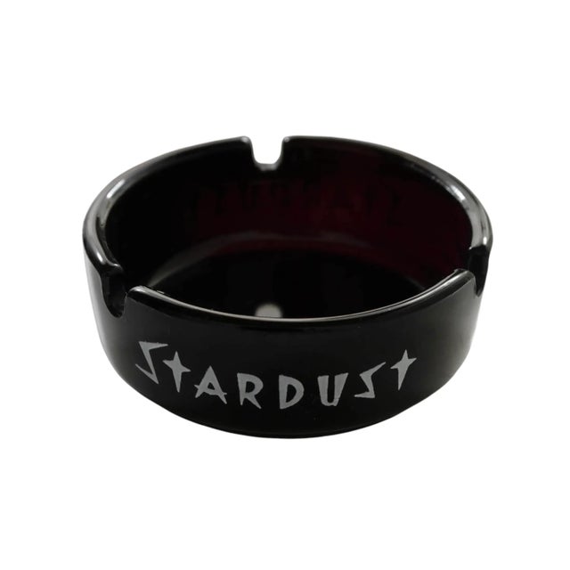 A black glass ashtray from the Stardust Hotel & Casino in Las Vegas, Nevada. Printed around the edge in white with the...