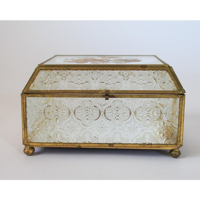 Vintage brass and glass trinket box with floral motif and mirrored bottom. No makers mark. One foot does have damage. It...