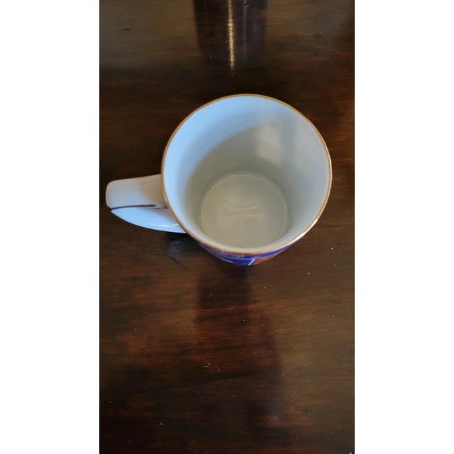 Set of 12 vintage ceramic mugs, each adorned with vibrant folk-inspired designs, showcasing a rich navy glaze punctuated...