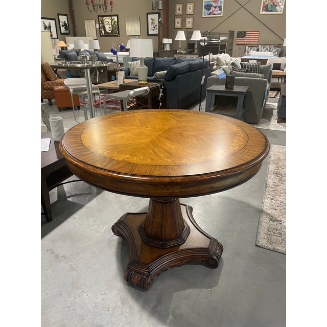 This round pedestal table features a veneered sunburst top with a decorative inlaid border. It stands on a fluted center...