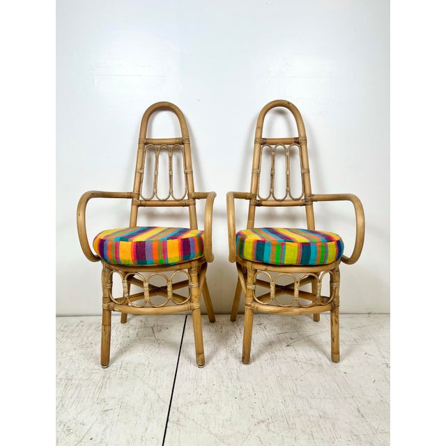 Vintage pair of rattan tall back arm chairs. High arched back with pencil reed accents. Curved arms. Removable cushions....