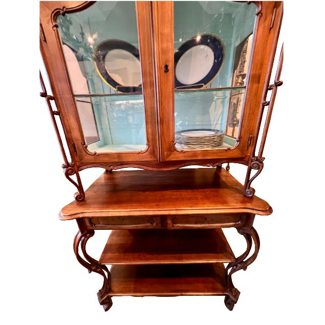 Two-part Queen Anne style etagere. Upper cabinet features interior glass shelf and operable lighting. Bottom features two...