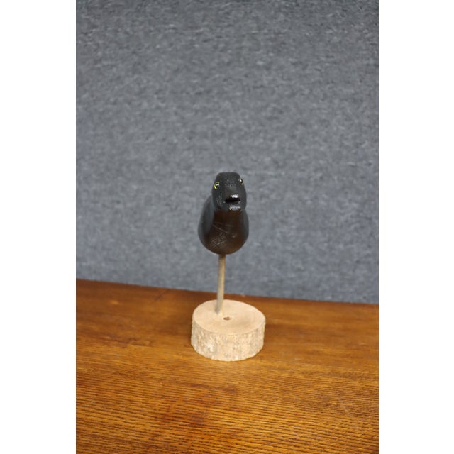 Early 20th century folk art crow with a carved wooden body, black painted finish, and yellow glass eyes. The bird features...