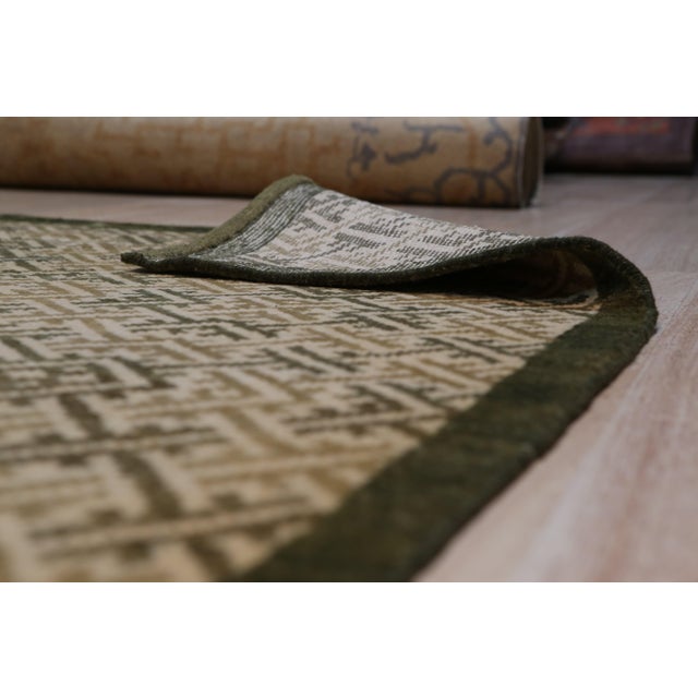 A 3' x 18' hand-knotted wool runner with an olive and gold interlocking geometric lattice inside a dark olive border....
