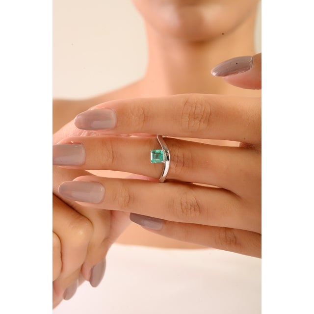 This elegant minimalist wave ring features a single square-cut emerald weighing approximately 0.63 carats, set in 14K...