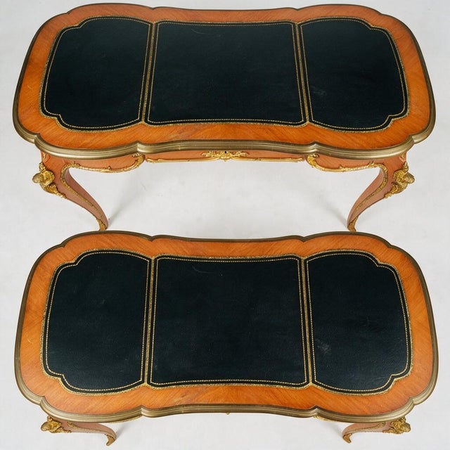 An elegant matching pair of French Louis XV style writing tables, combining warm wood veneers, gold-tooled black leather...