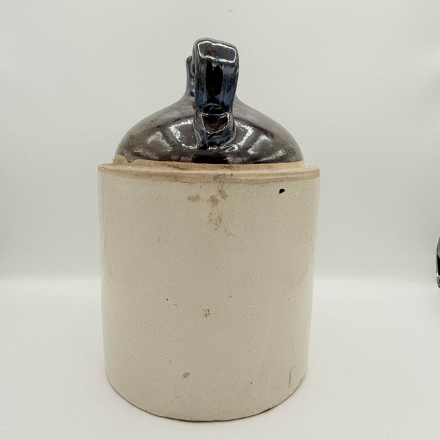 A classic American stoneware moonshine or whiskey jug, finished with a rich dark Albany slip-style glaze over a natural...