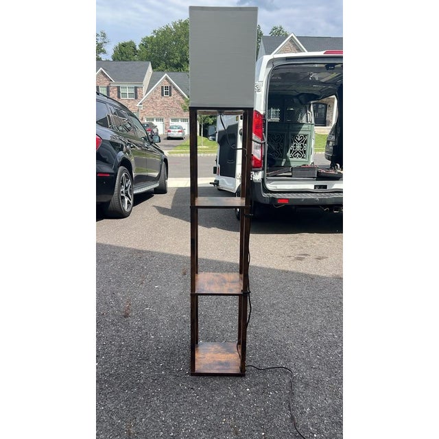 Contemporary dark wood floor lamp featuring three built-in display shelves and a clean white fabric shade. A great space-...