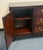 Elegant Asian-inspired sideboard featuring a rich, dark wood finish with beautifully figured panels and warm brass...