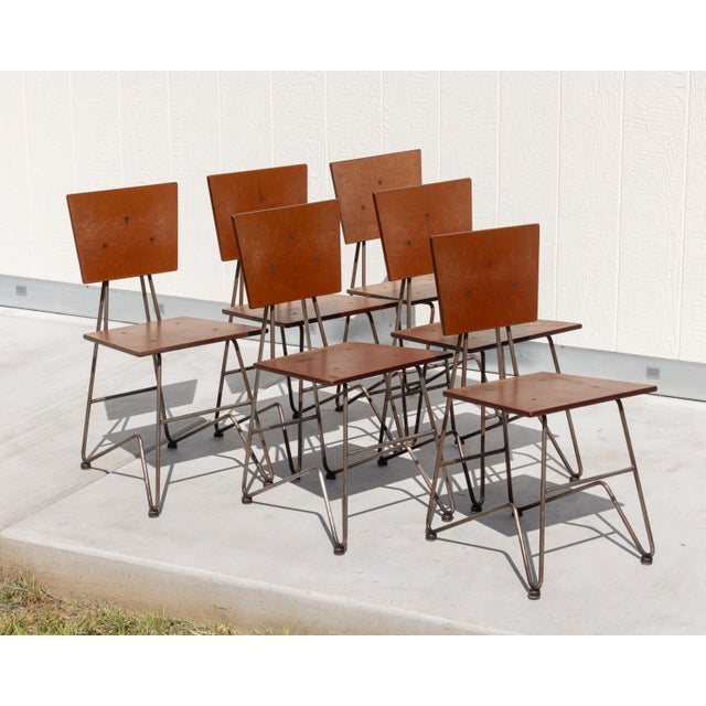 Set of six industrial dining chairs constructed from resin-coated composite panels and bent steel, reflecting the...