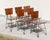 Set of six industrial dining chairs constructed from resin-coated composite panels and bent steel, reflecting the...