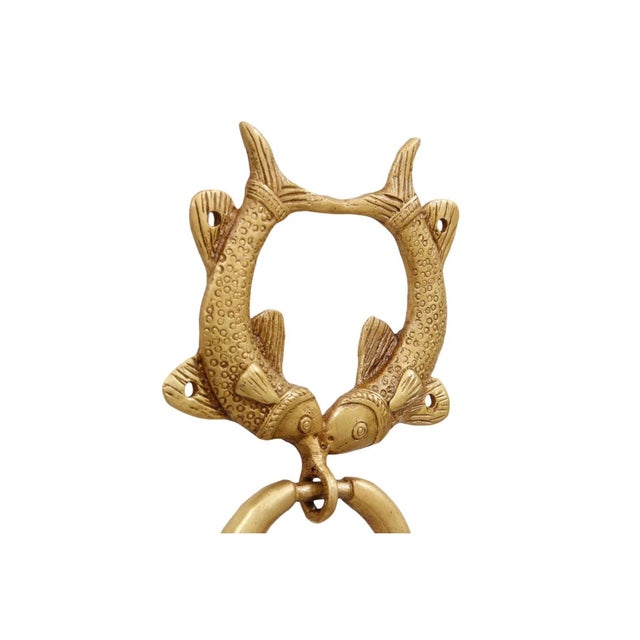 A gold brass door knocker shaped like a pair of fish. The double fish symbol is intended to bring prosperity and is...