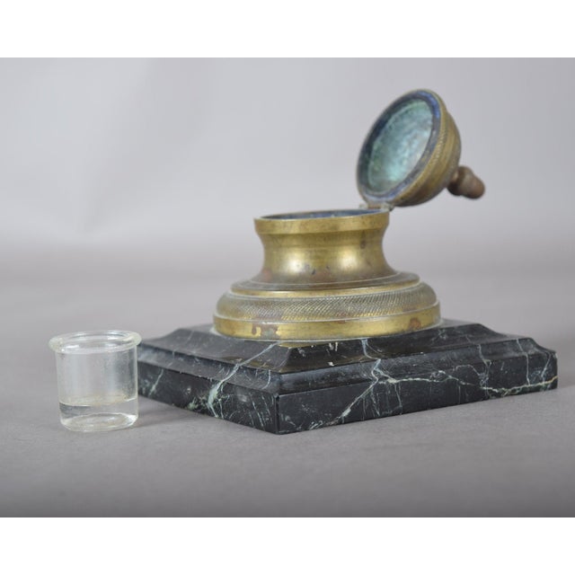 19th-century bronze inkwell with a hinged domed lid, mounted on a square dark marble base. The small removable ink insert...