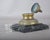 19th-century bronze inkwell with a hinged domed lid, mounted on a square dark marble base. The small removable ink insert...