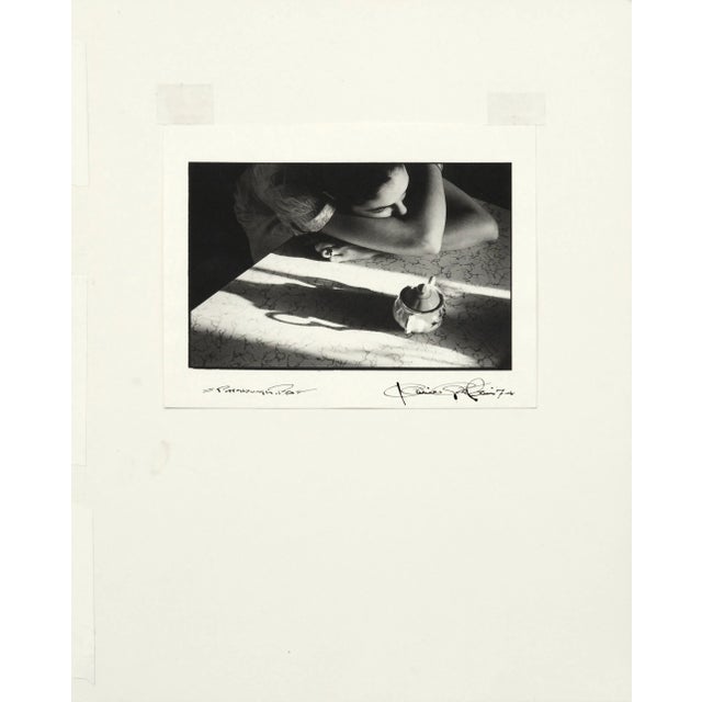 Compelling 1970s black and white photograph of a contemplative woman leaning on a table into her crossed arms, beside a...