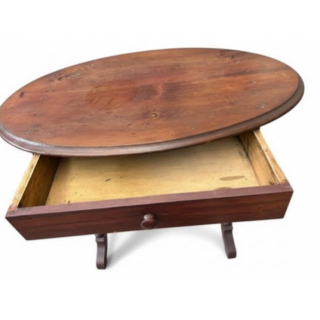 Charming antique oval occasional table featuring an expressive aged wood surface, a single functional drawer, and an...