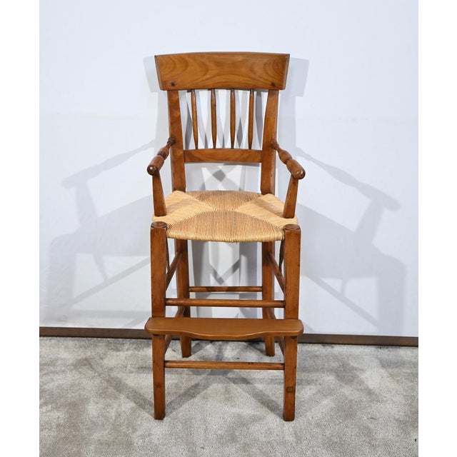 This high chair rests on two square-section front legs, tapering downwards and held in place by two rungs and a curved...