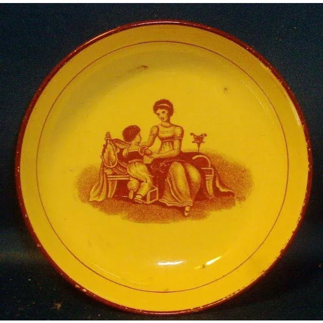 A diminutive pearlware plate featuring a classical scene of a mother and child in a puce palette. Measures 4" in diameter...