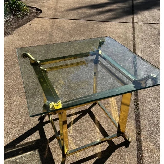 Square Hollywood Regency table with substantial brass base and beveled glass top with scrolled details.