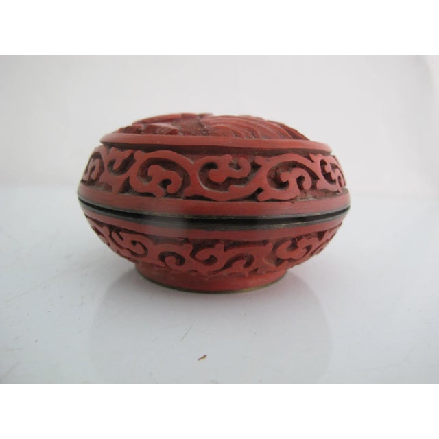 Chinese cinnabar lacquerware box with lid. Round with carved figural scene on lid and scrolling design at side. Interior...