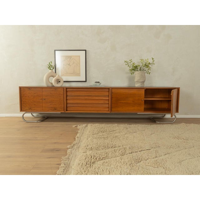 A unique sideboard from the 1960s. Its walnut veneer body features three drawers, four doors, two shelves, and new...