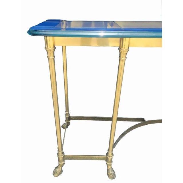 A beautiful vintage solid brass glass top console table with hooved feet. The table features a brass frame with curved...